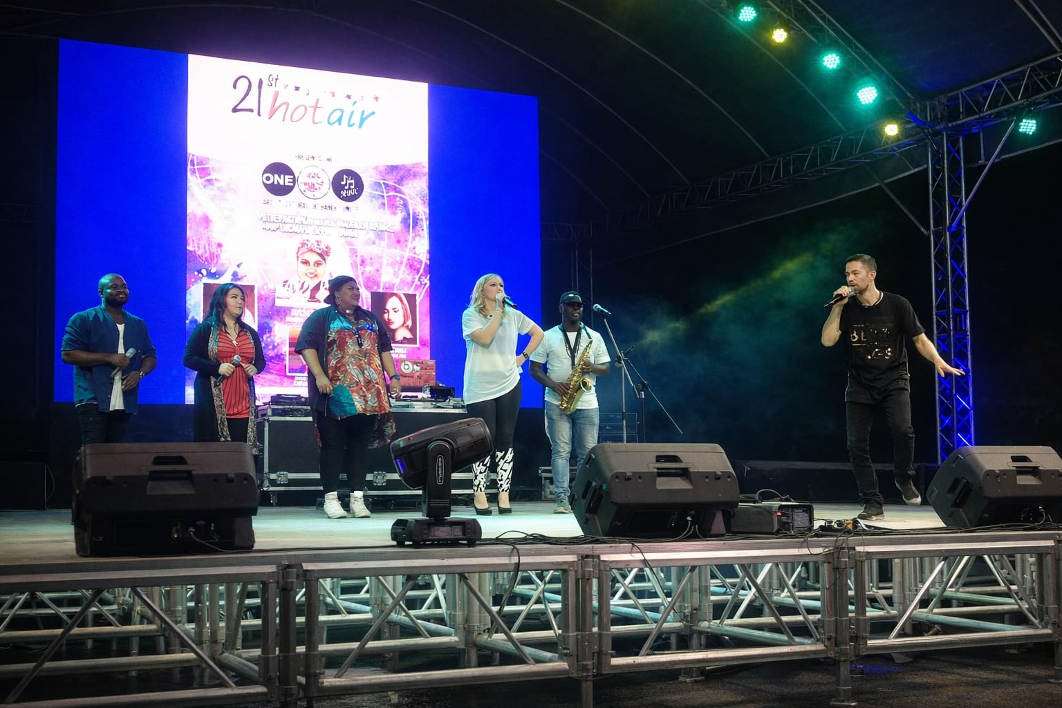 Clinton Mann performing on an outdoor stage with a band and backing singers